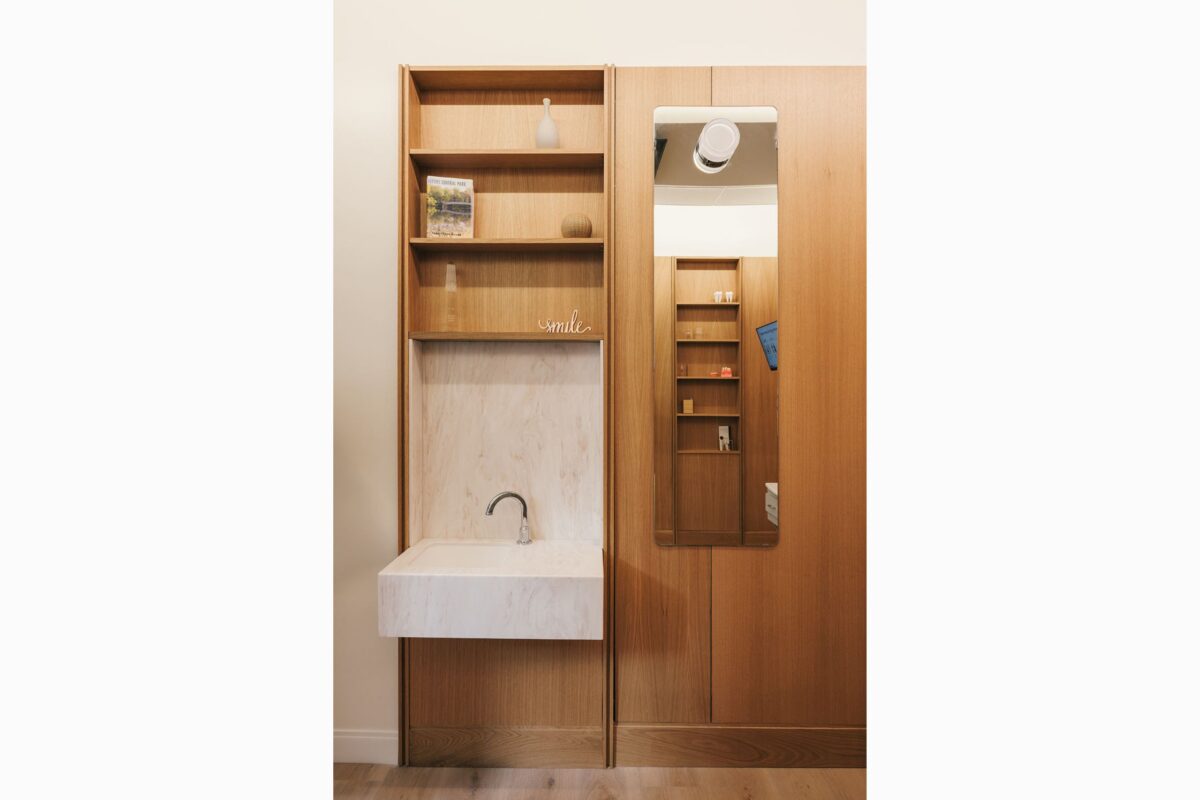 Built-in wood cabinet featuring open shelves with decor, a small white sink with a chrome faucet, and a vertical mirror.